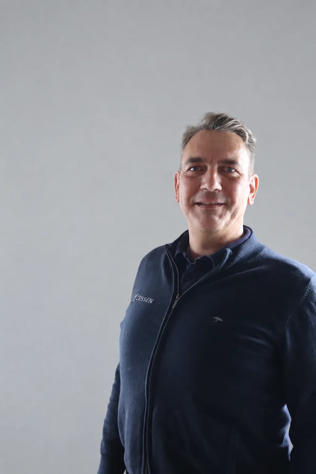 Porträt von Michael Scheffold in dunkelblauer Strickjacke vor hellgrauem Hintergrund